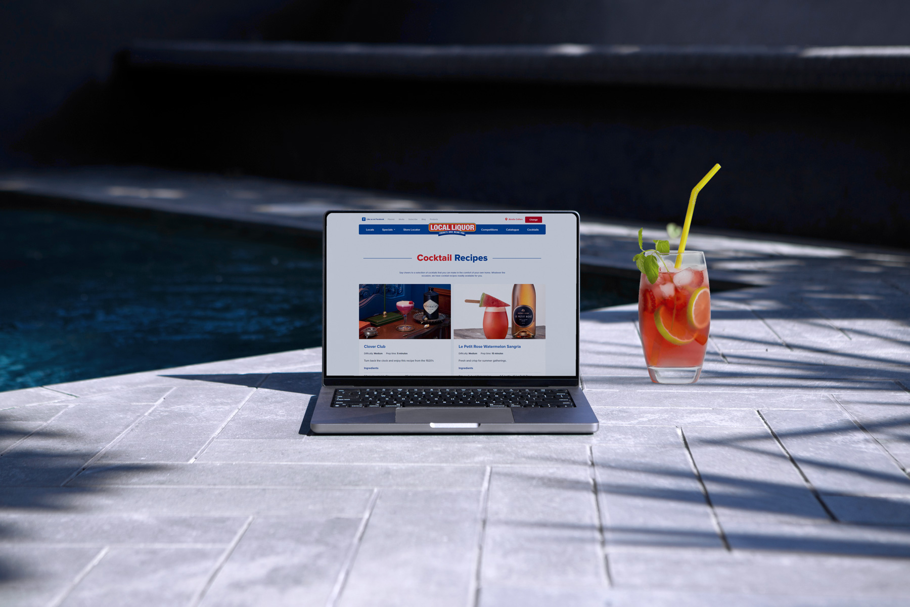 A poolside laptop beside a cocktail. The laptop shows the Local Liquor website.