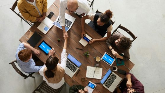 A group of coworkers sat around a wooden table with their laptop open.