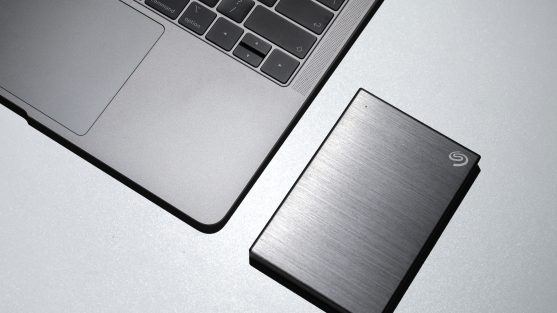 A laptop sits on a table with an external hard drive, perfect for website backup, placed next to it. The hard drive features a brushed metallic finish, adhering to the best practices for data storage in 2024.